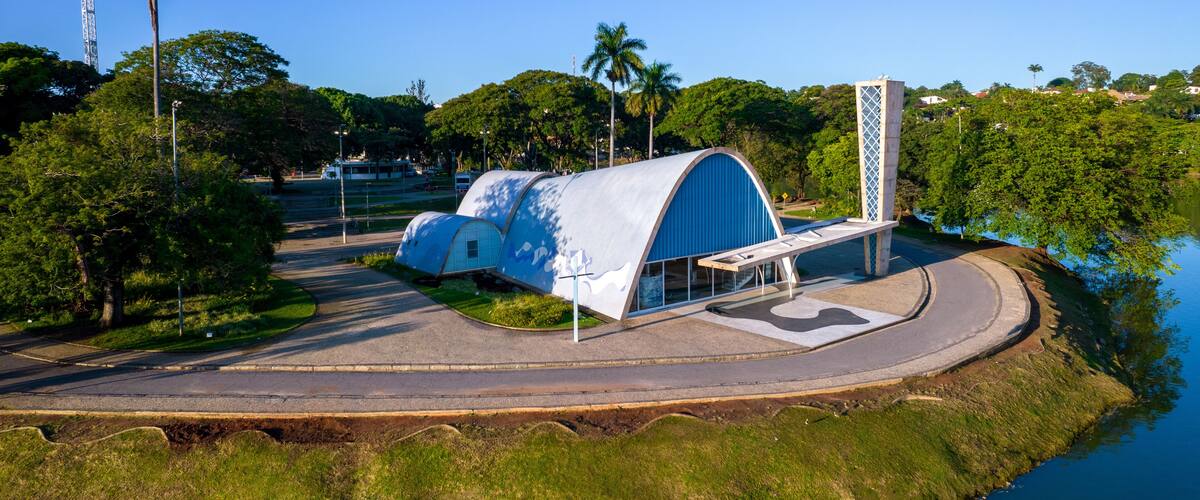 A modern architectural structure with a blue dome and a tall white tower, surrounded by lush greenery and a body of water.