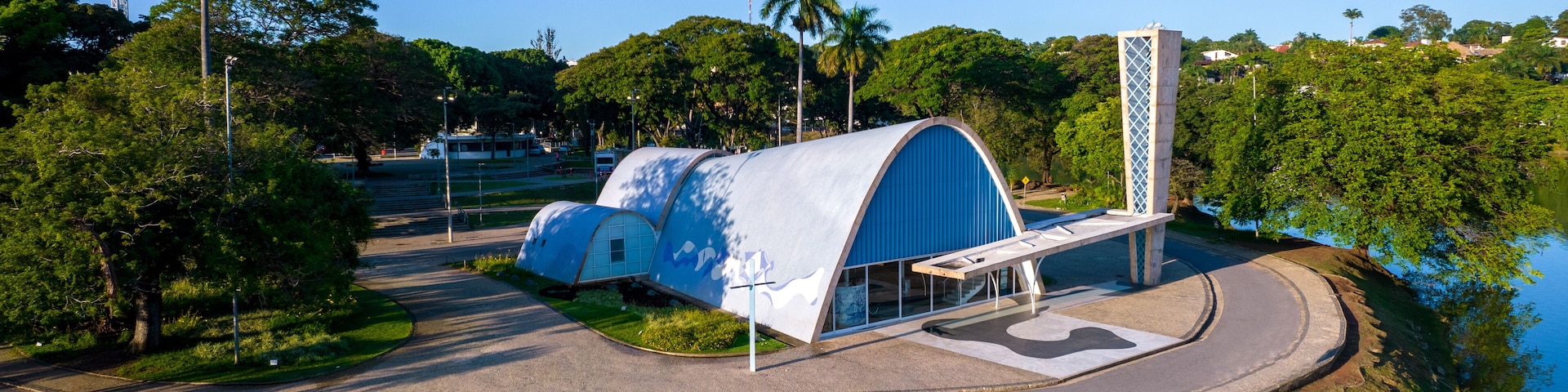 A modern architectural structure with a blue dome and a tall white tower, surrounded by lush greenery and a body of water.