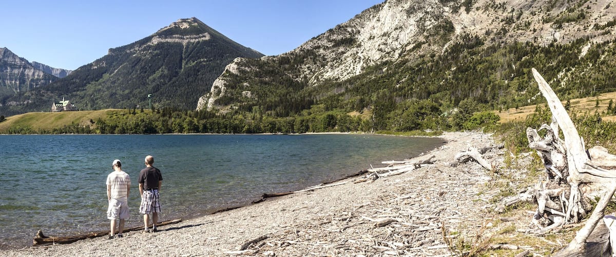 A lake surrounded by mountains, a wooden structure on the shore, and a person standing by the water.