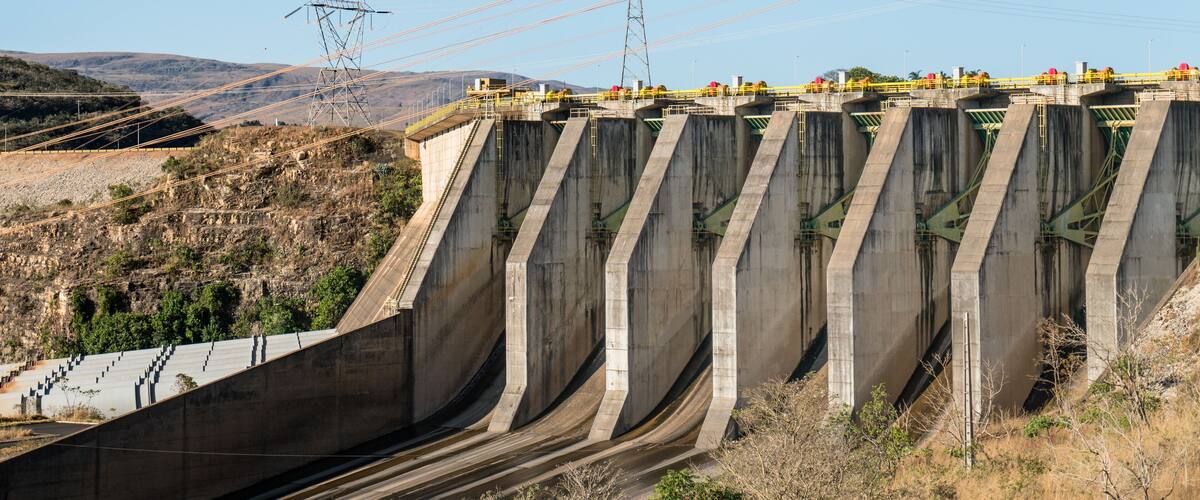 A large concrete dam with multiple spillways and power lines in the background.