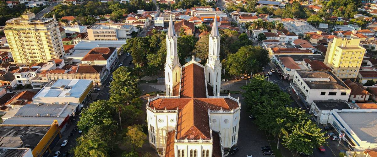 An aerial view of a city with a prominent church featuring two tall spires and a red-tiled roof, surrounded by residential buildings and greenery.