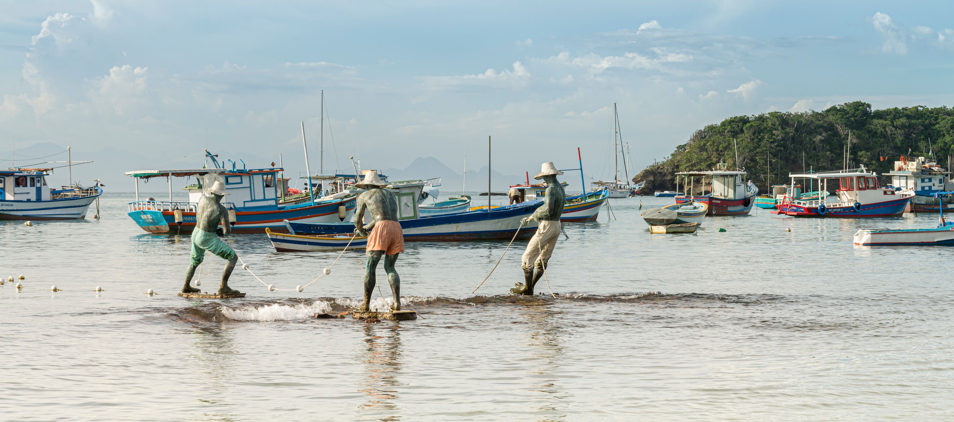 A harbor with several boats, some anchored and some in the water, and a few people standing in the water.