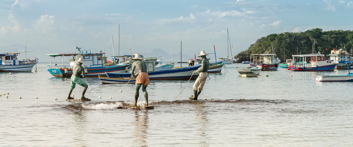 A harbor with several boats, some anchored and some in the water, and a few people standing in the water.