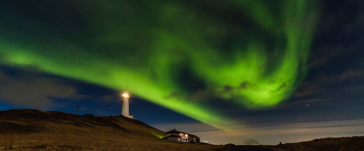 A lighthouse on a hill with the Northern Lights in the sky.