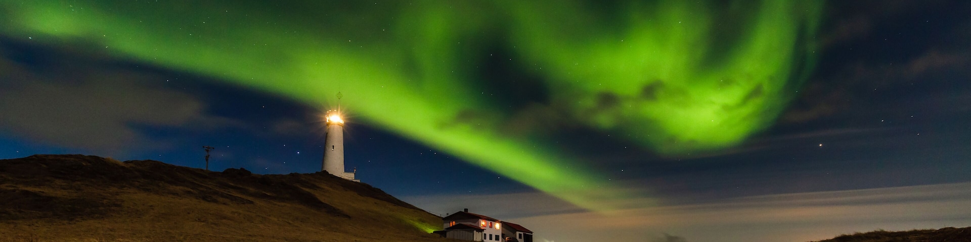 A lighthouse on a hill with the Northern Lights in the sky.