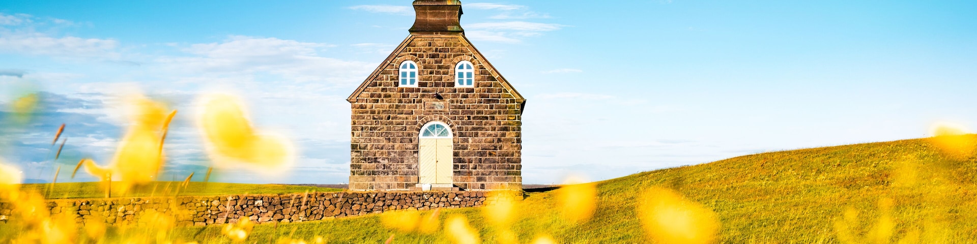 Uma igreja com um campanário, cercada por um campo gramado com flores amarelas.