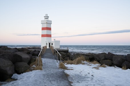 Ein Leuchtturm mit einem rot-weiß gestreiften Turm, ein Betonweg, der dorthin führt, und eine felsige Küstenlinie mit dem Ozean im Hintergrund.