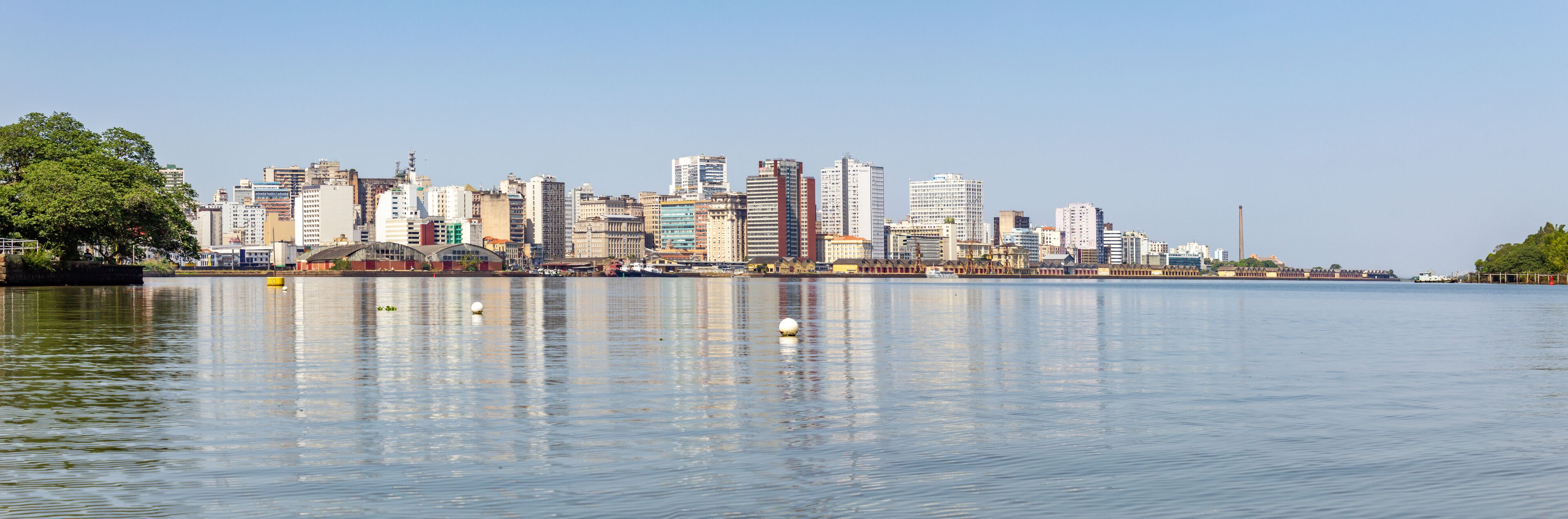 A city skyline with tall buildings reflected in calm water.