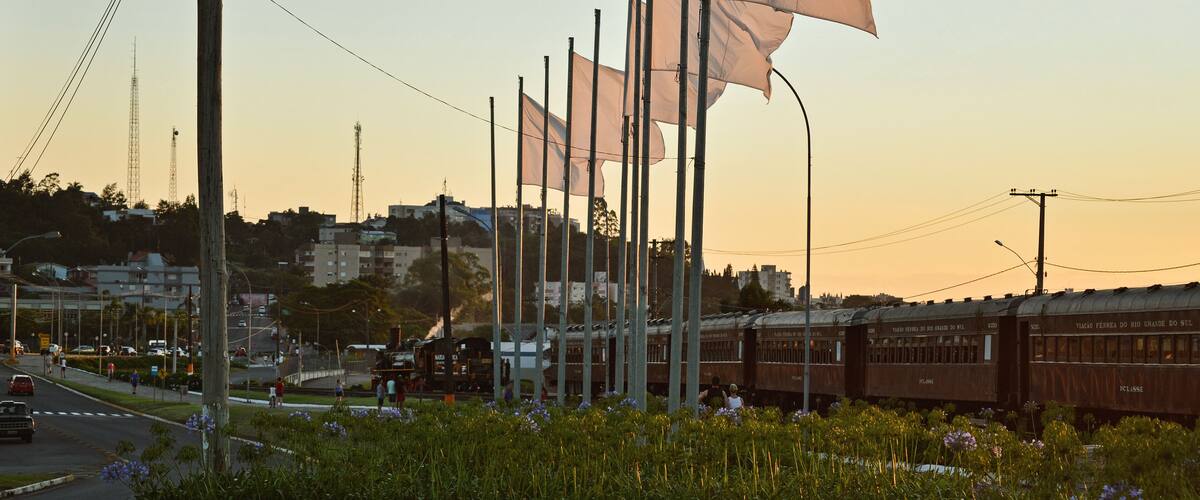 A train station with flags, a train, and a cityscape in the background.