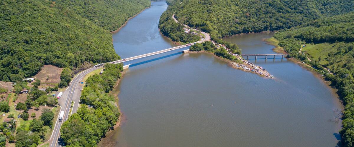 A river with a bridge and surrounding forested hills.