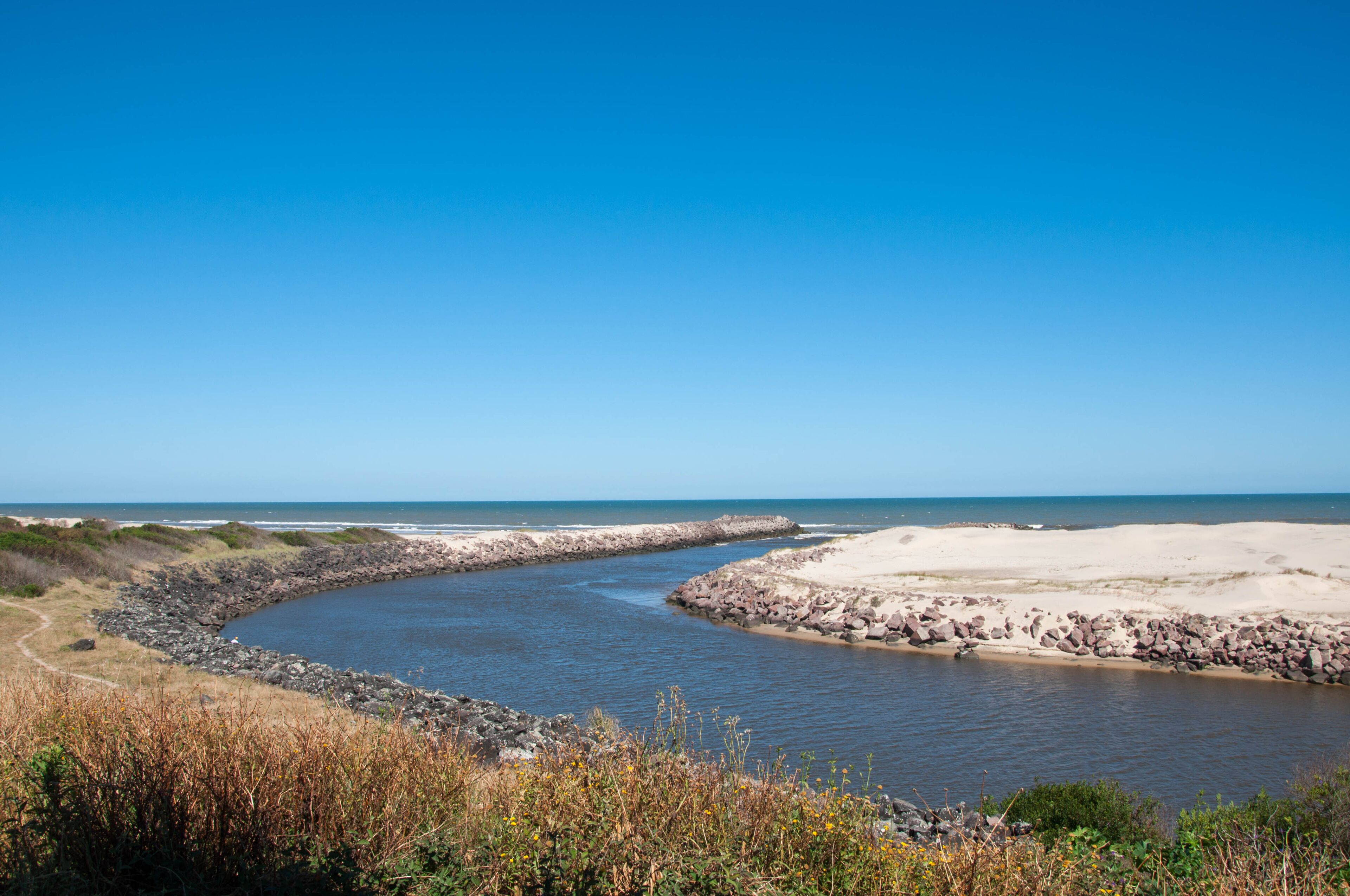 A coastal landscape with a curving river, sandy beach, and rocky shoreline.