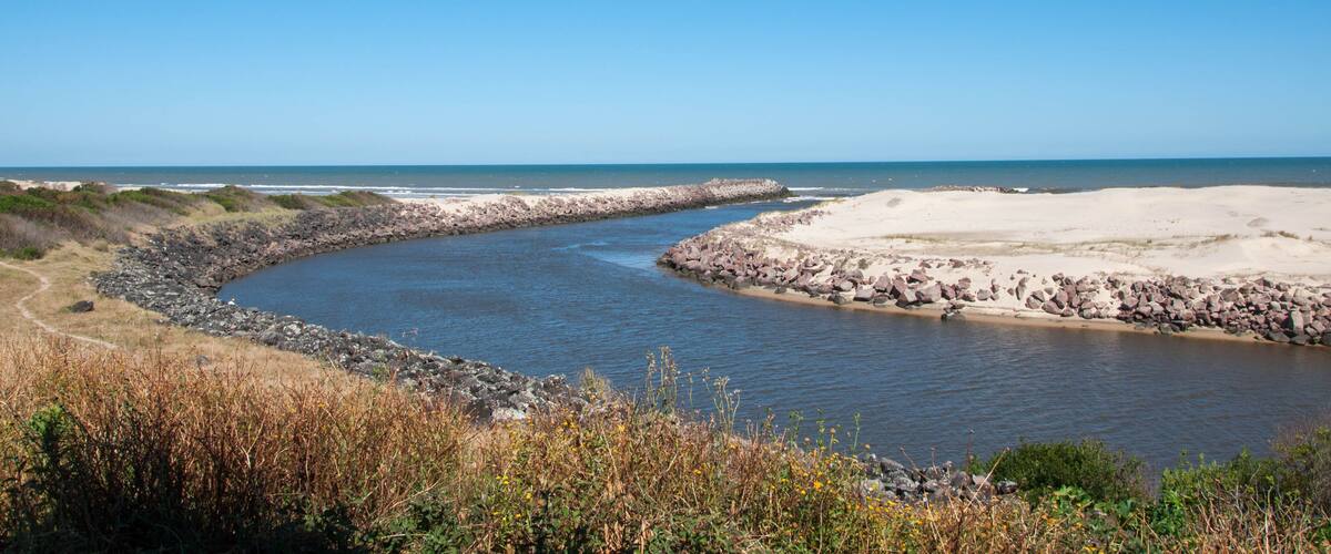 A coastal landscape with a curving river, sandy beach, and rocky shoreline.