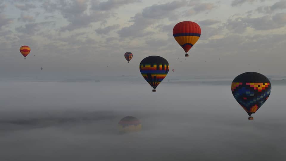 A group of colorful hot air balloons floating above a foggy landscape.