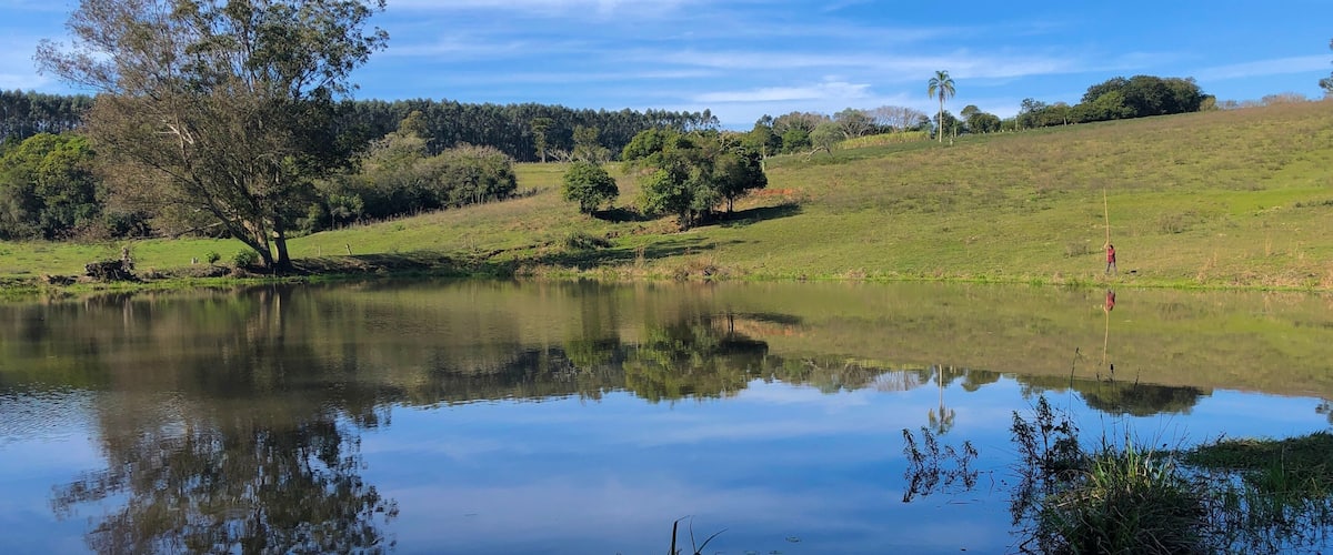 A calm lake surrounded by trees and a grassy hill.