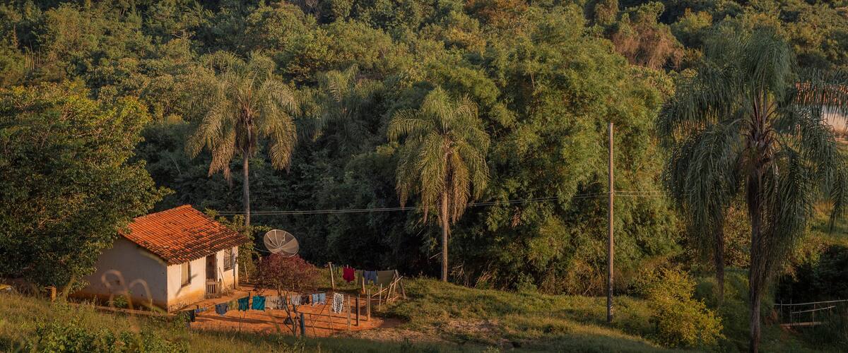 A rural landscape with a small house, lush greenery, and distant hills.