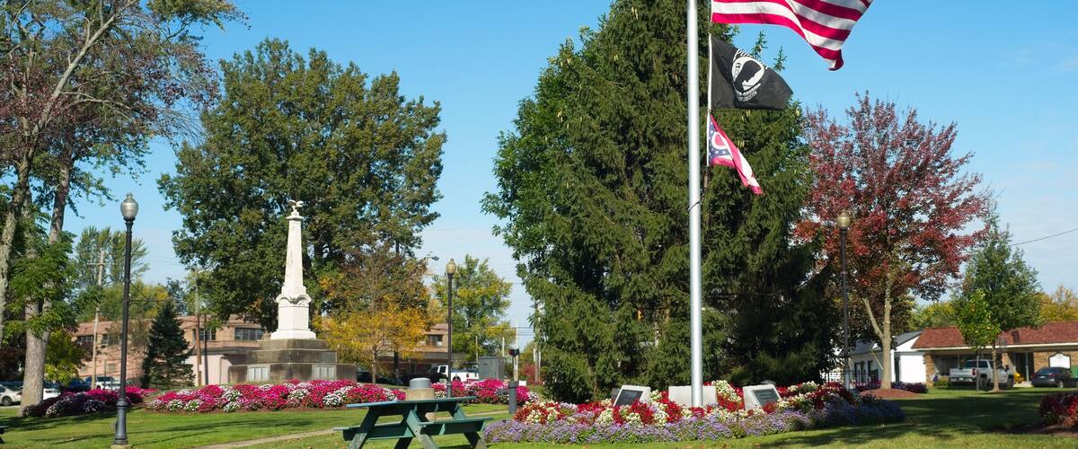 A park with a flagpole, a monument, and picnic tables.