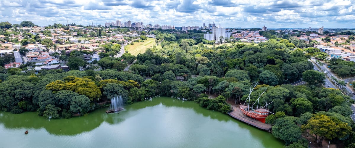 A large green lake surrounded by dense trees and a cityscape in the background.