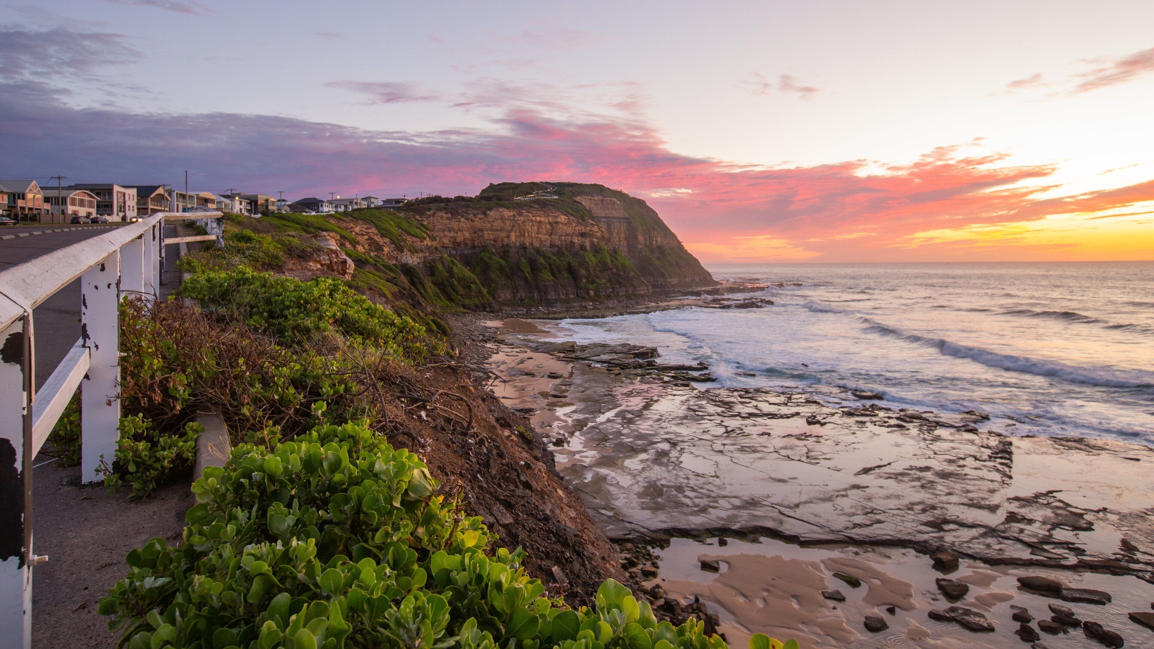 Paisagem costeira com penhasco, praia e uma passarela.