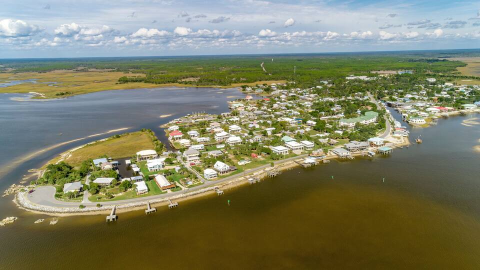 An aerial view of a coastal town with a marina, houses, and a river.