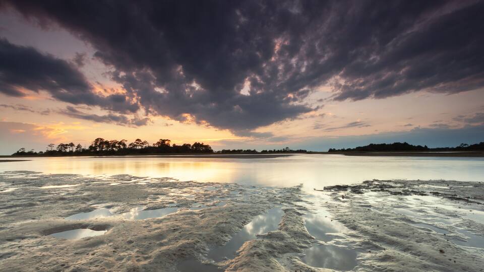 A calm lake at sunset with a cloudy sky.