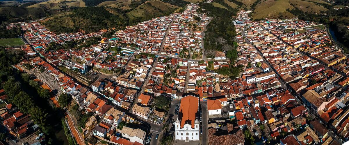 An aerial view of a densely packed town with red-roofed buildings, a prominent white church, and surrounding green hills.