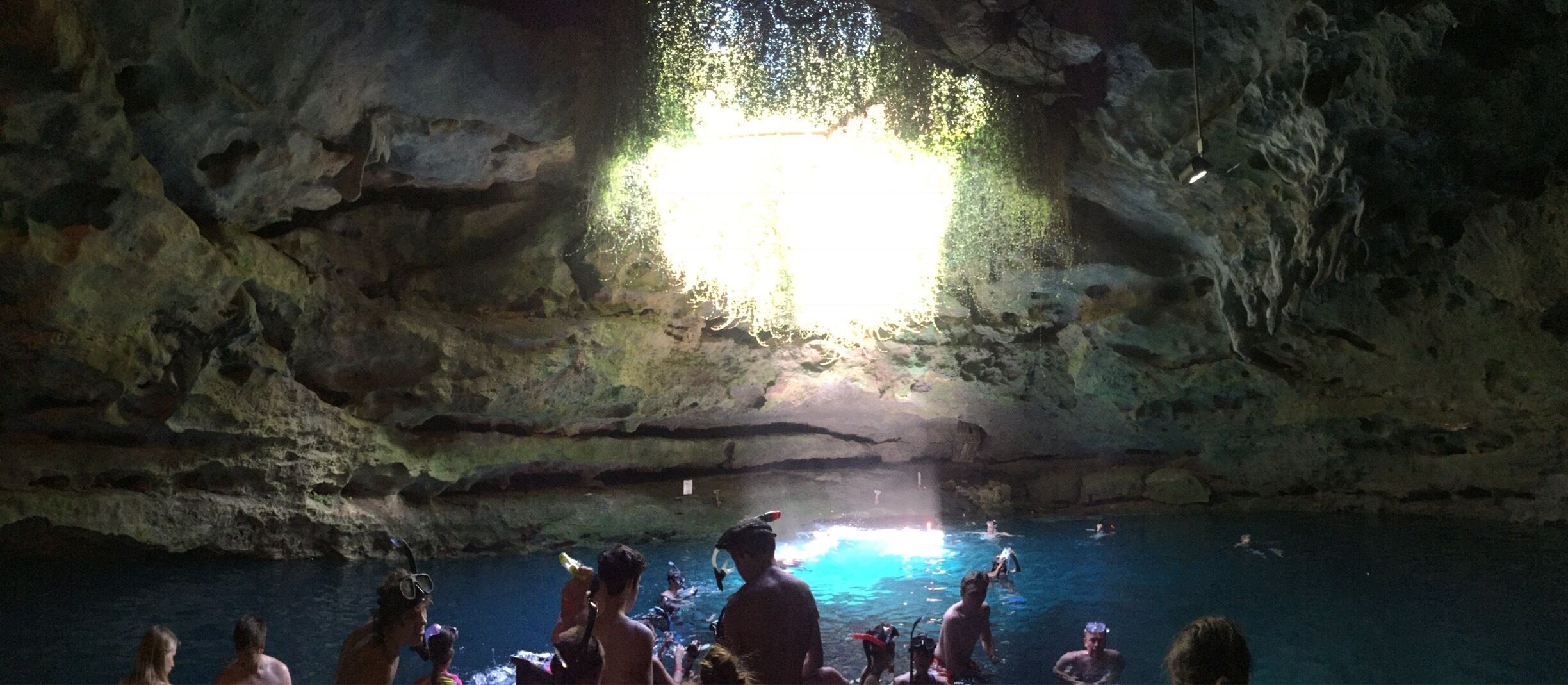 A cave with a bright light at the center and people swimming in the water.