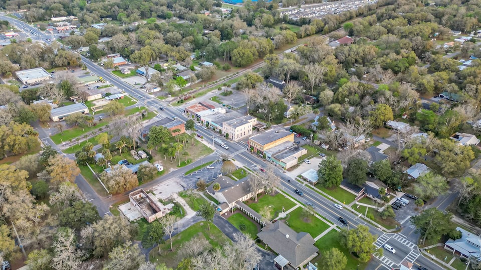An aerial view of a suburban area with a mix of residential houses, commercial buildings, and a large parking lot.
