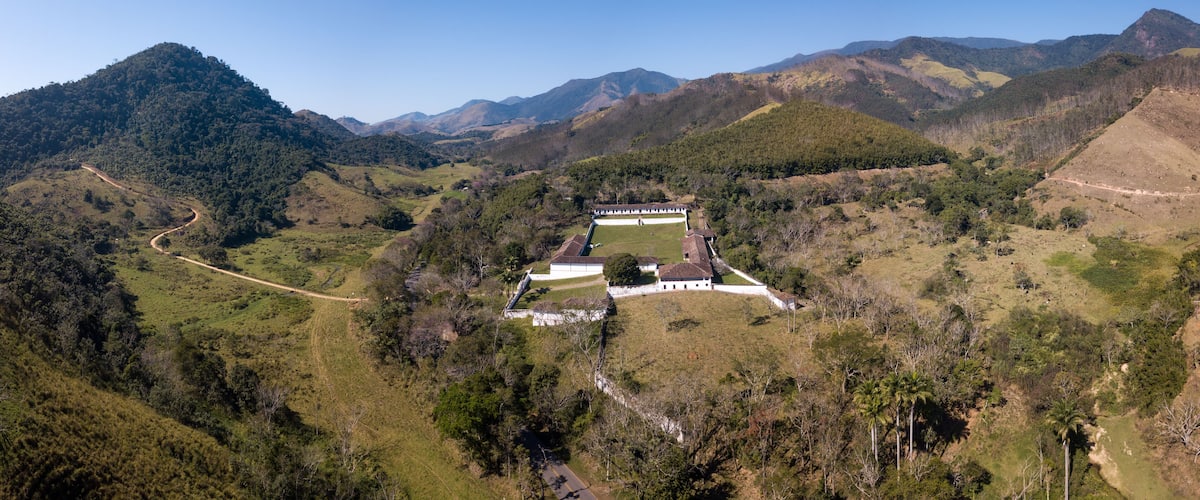 A mountainous landscape with a white building complex surrounded by lush greenery and a winding road.