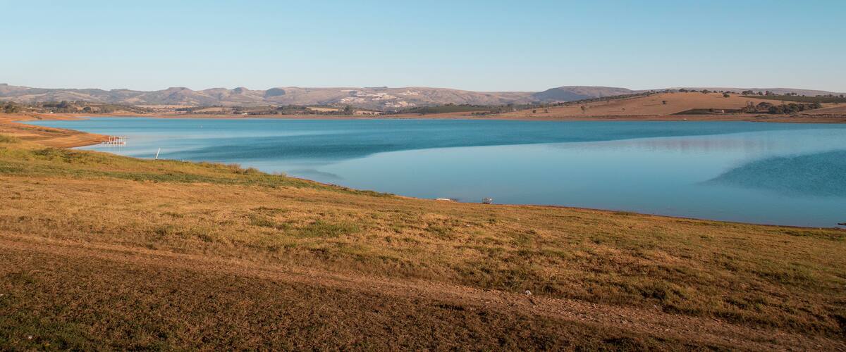 A calm lake surrounded by rolling hills and a clear blue sky.