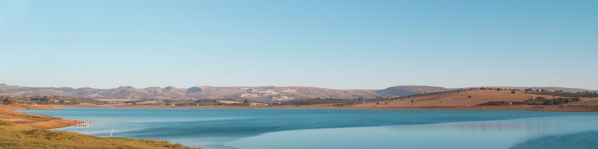 A calm lake surrounded by rolling hills and a clear blue sky.