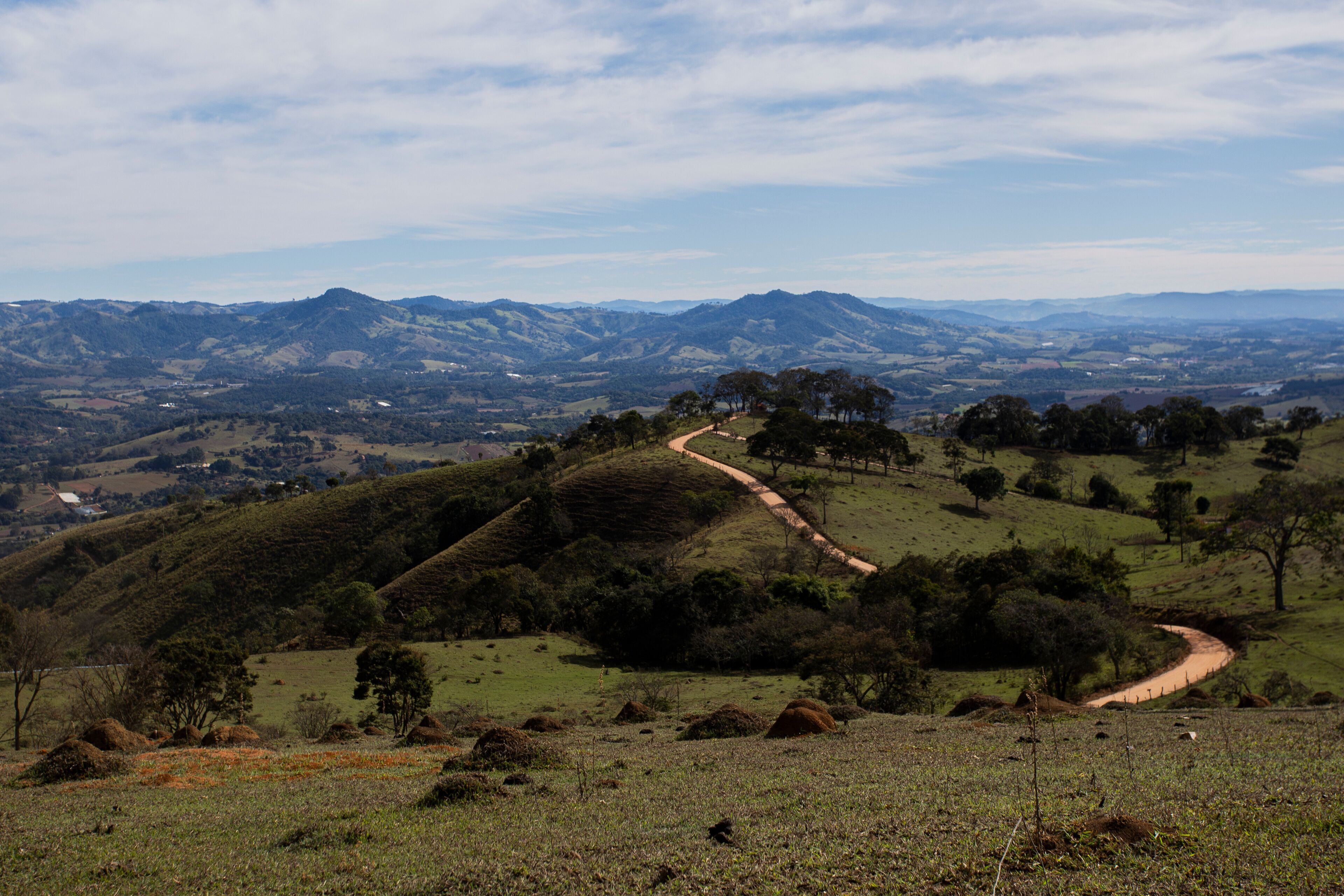 A winding dirt road through rolling hills with distant mountains under a partly cloudy sky.