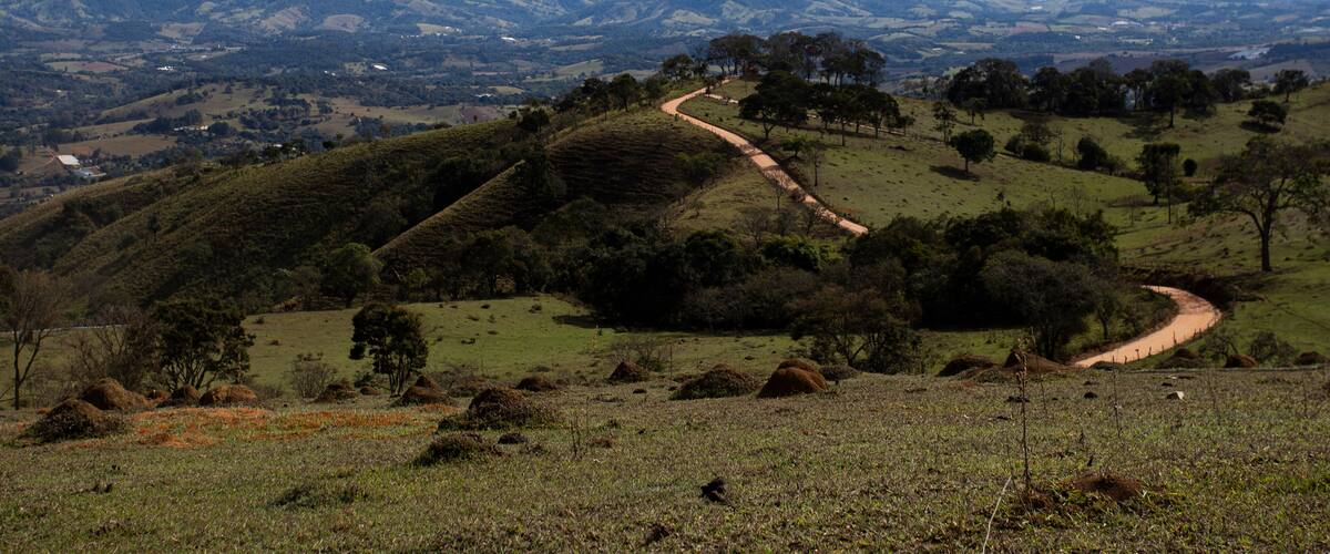 A winding dirt road through rolling hills with distant mountains under a partly cloudy sky.