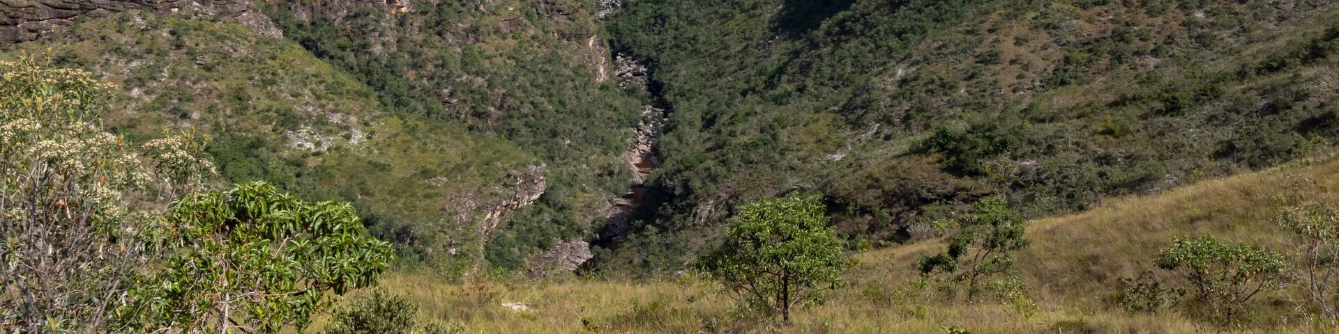 A canyon with a waterfall, steep cliffs, and surrounding greenery.