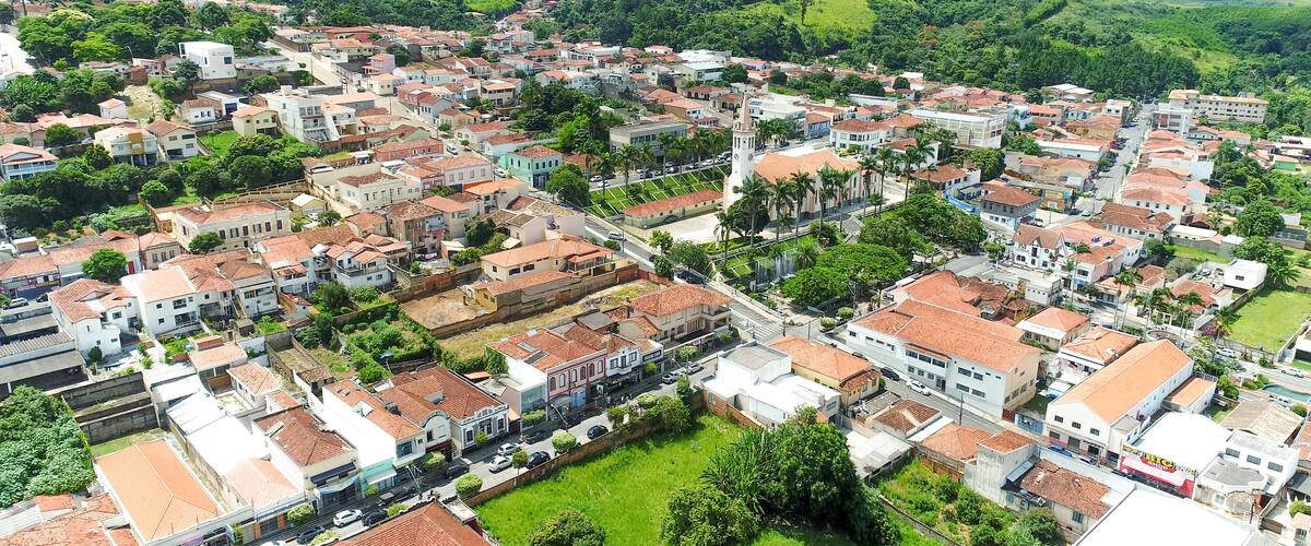 An aerial view of a town with red-roofed buildings, surrounded by lush green hills and mountains.