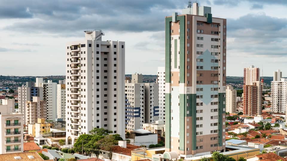 A cityscape with a mix of high-rise buildings and traditional houses, under a cloudy sky.