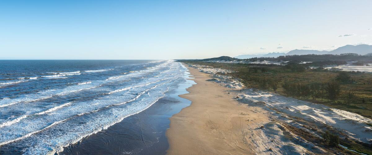 A beach with waves, a sandy shore, and distant mountains.