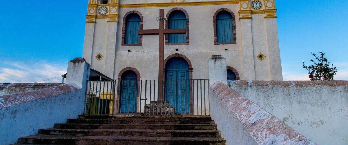 A historic church with a large cross, two bell towers, and a staircase leading to the entrance.