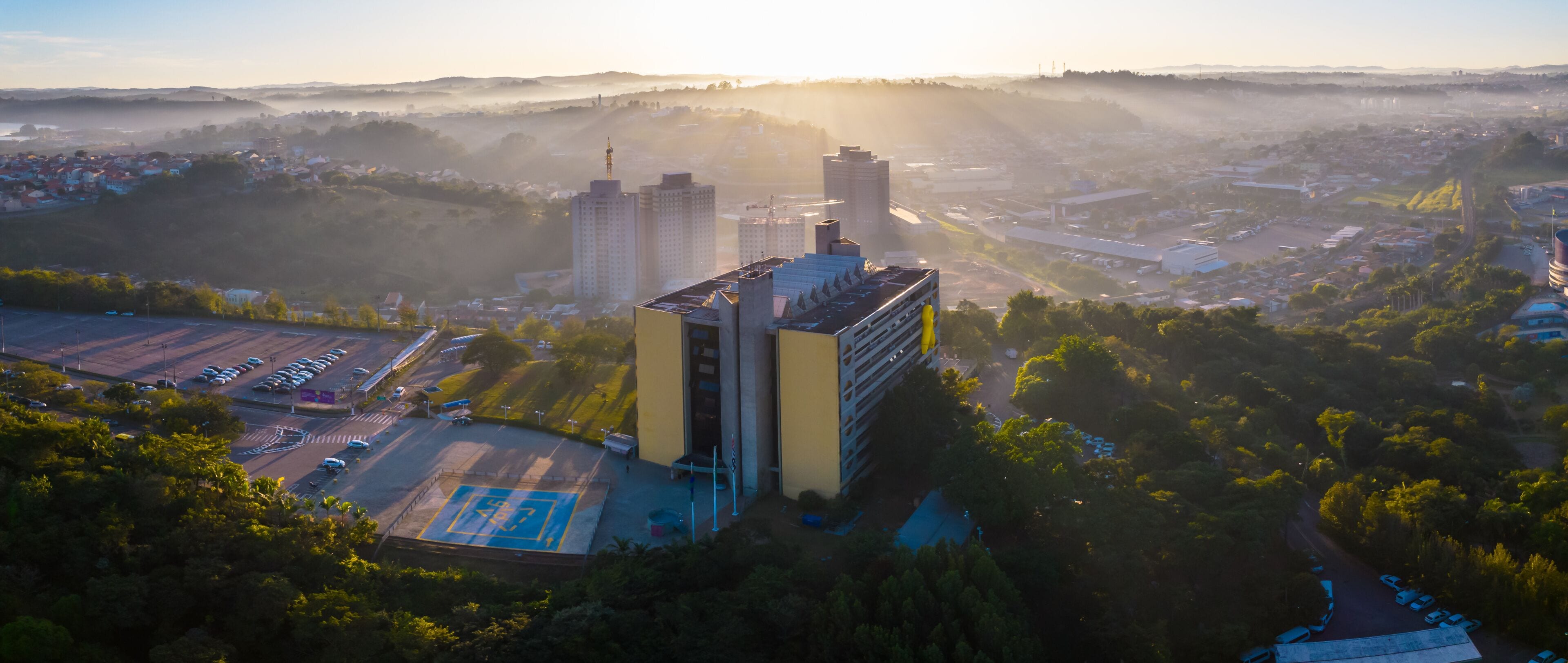 A cityscape with a prominent yellow building, a parking lot, and surrounding greenery.