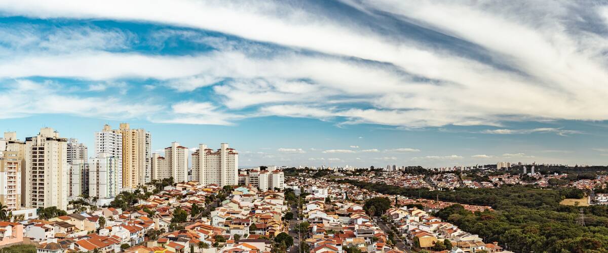 A cityscape with high-rise buildings, a densely packed residential area, and a clear sky with clouds.