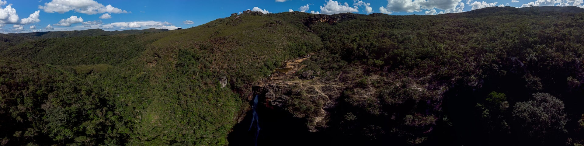 A mountainous landscape with a waterfall and dense forest.