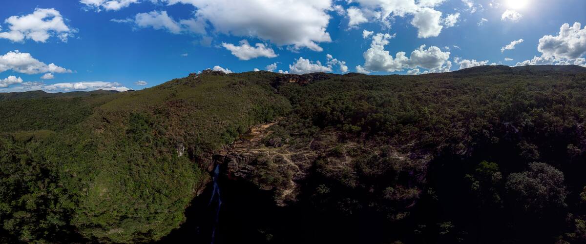 A mountainous landscape with a waterfall and dense forest.