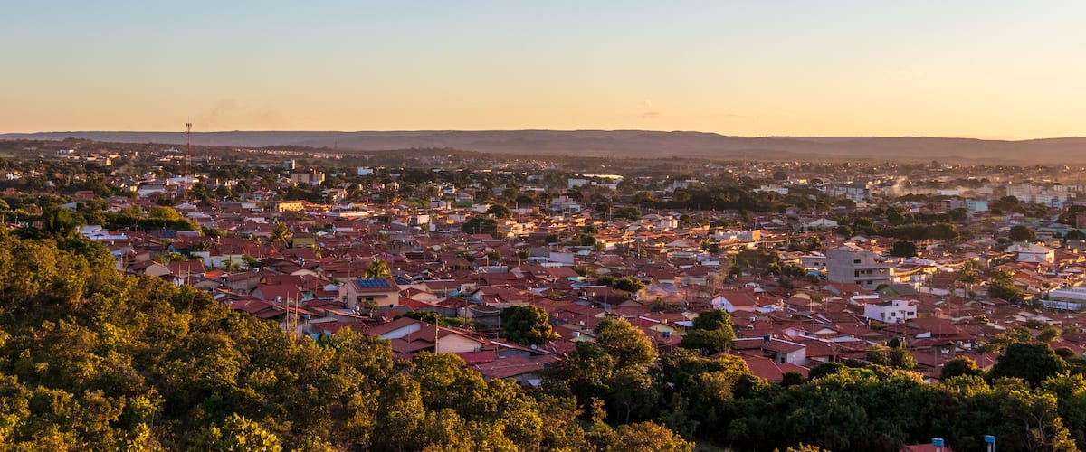 A cityscape with red-roofed buildings and green trees, under a clear sky.