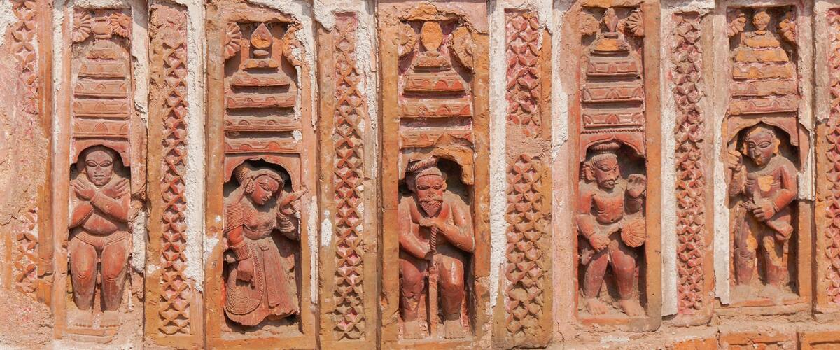 A series of intricately carved stone figures in a row, each depicting a different pose and attire, set within a textured wall.