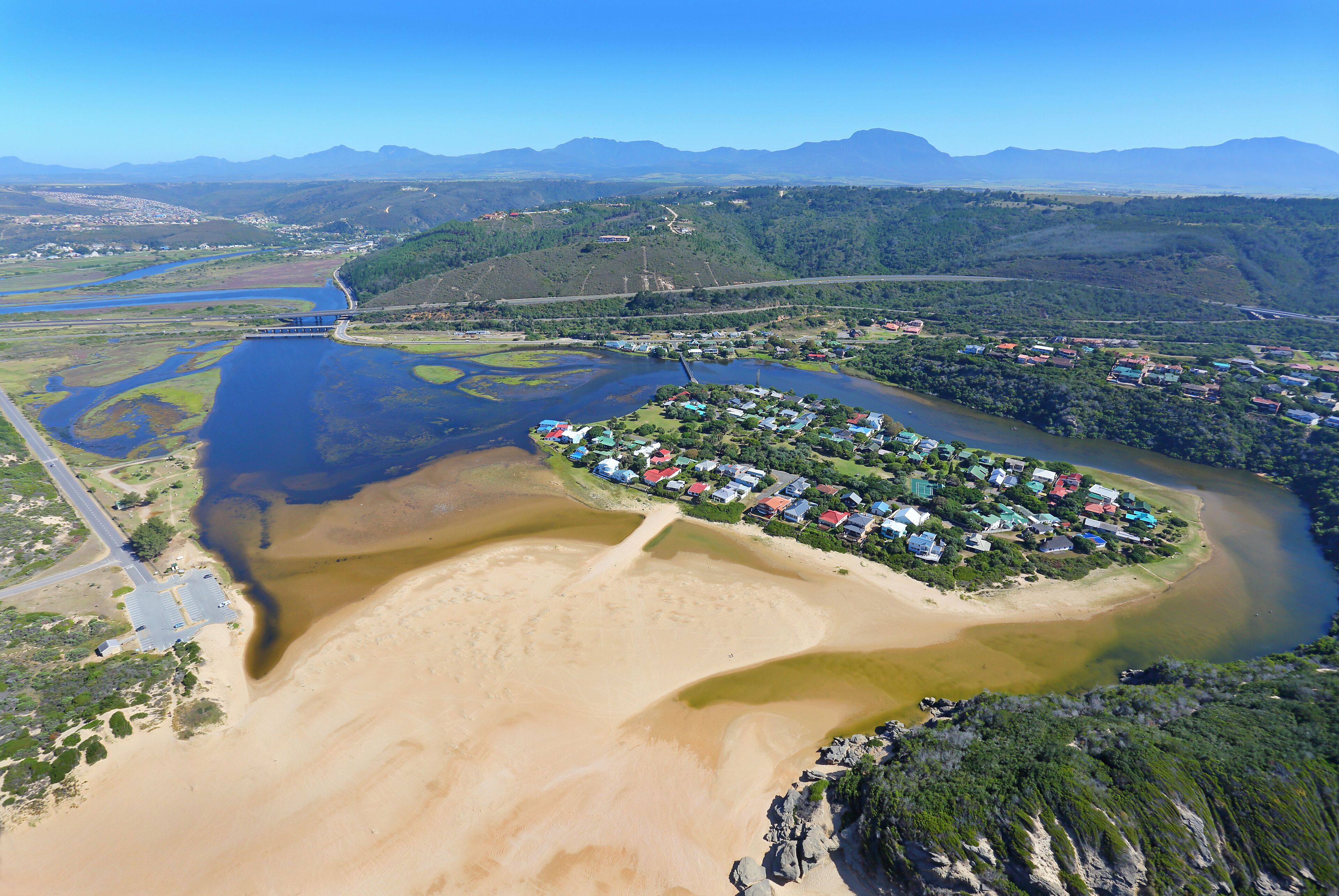 An aerial view of a coastal area with a river, a bridge, and a residential community.