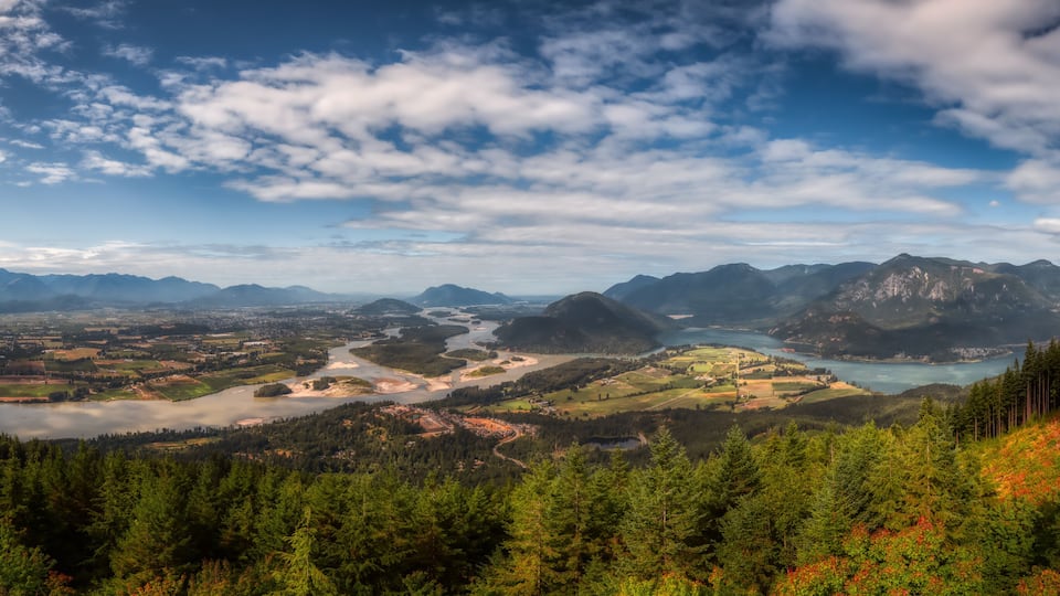 A mountainous landscape with a river, dense forests, and a distant town.