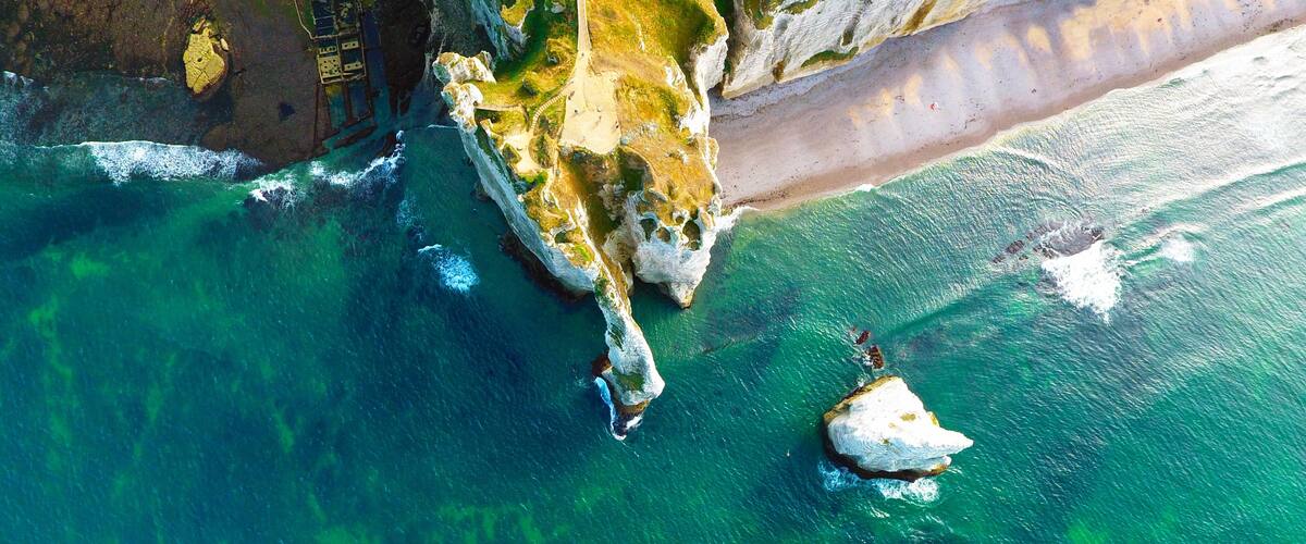 A coastal landscape with clear turquoise waters, rocky cliffs, and a sandy beach.