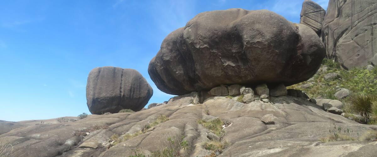 A rocky landscape with large boulders and sparse vegetation under a clear blue sky.