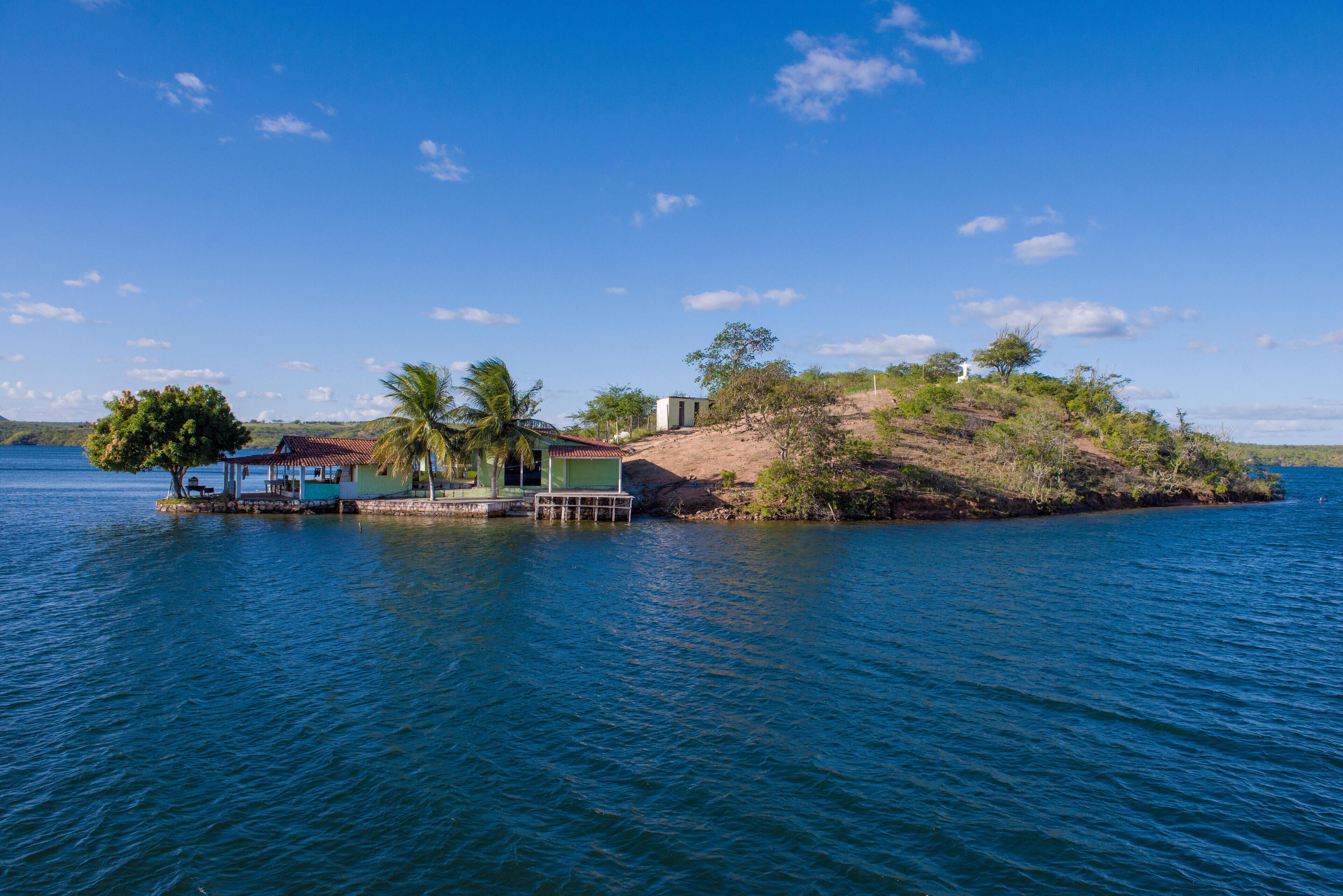 A small island with a gazebo, palm trees, and a house by the water.