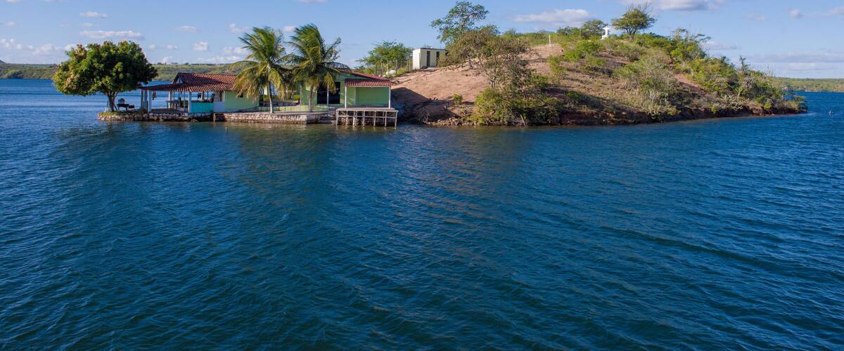 A small island with a gazebo, palm trees, and a house by the water.