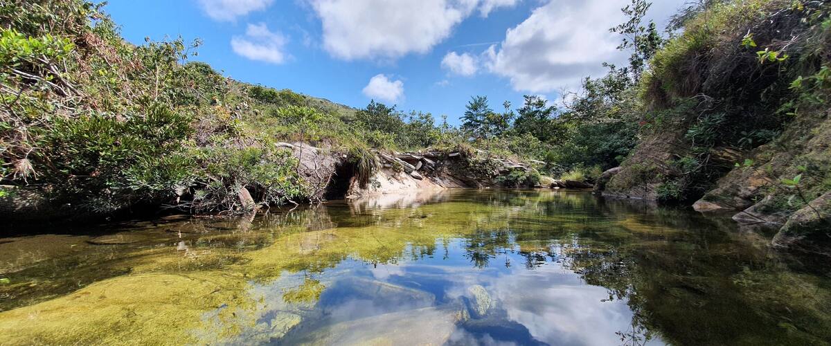 A clear river surrounded by dense greenery and rocky terrain.